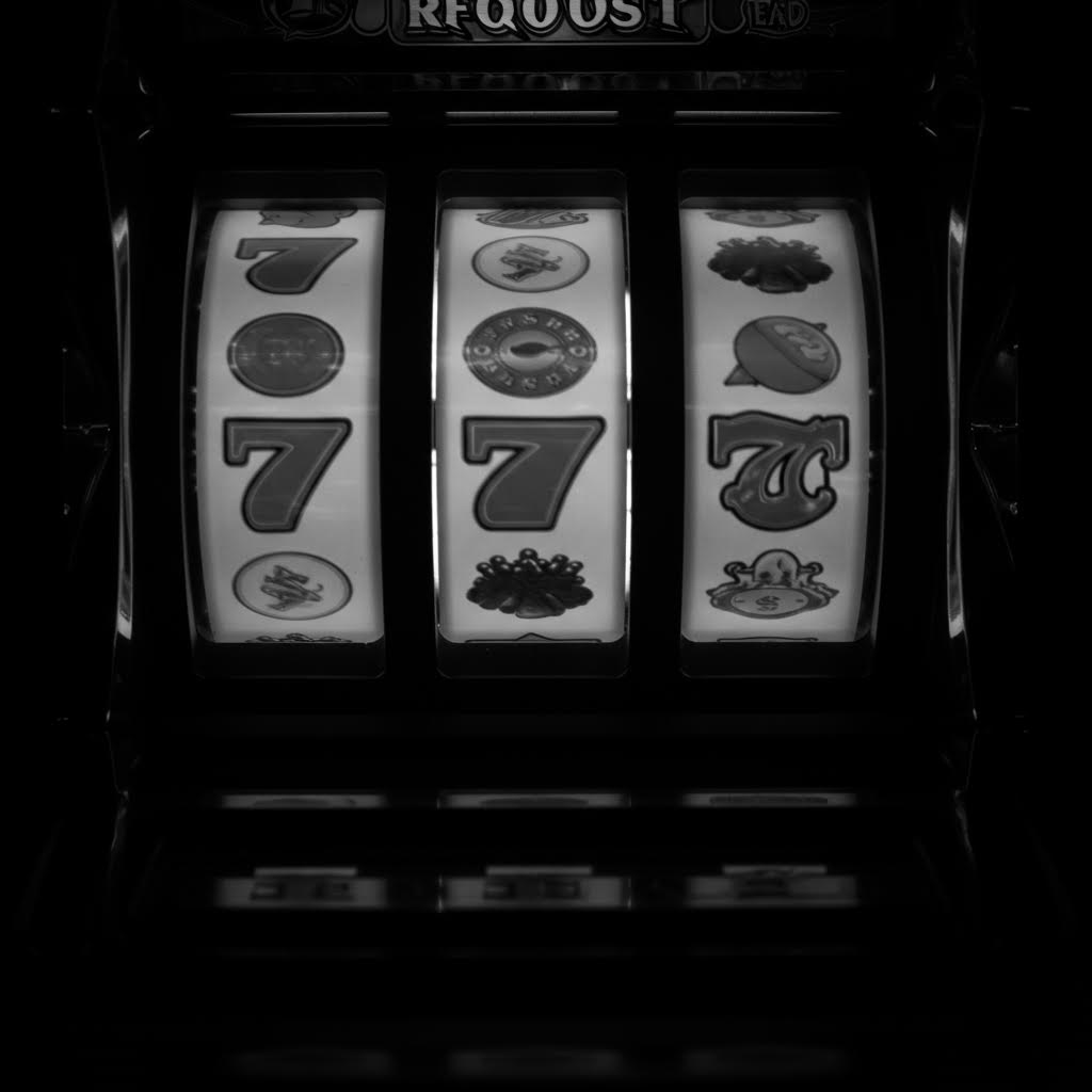 어두운 배경 속 슬롯머신 릴에 숫자 7과 상징 아이콘이 정렬된 모습의 흑백 이미지